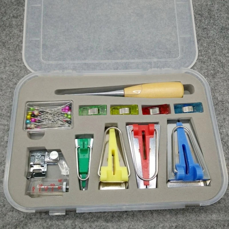 A clear plastic storage box containing a set of professional sewing bias binder tools including needles and various metal too