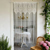 Vintage lace tassel door curtains hanging in a white door frame with a table and greenery visible.