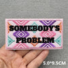 Pink embroidered patch with black text reading Somebody's Problem on a light pink fabric background