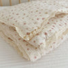 A stack of white muslin blankets with a delicate floral print resting on a white surface.