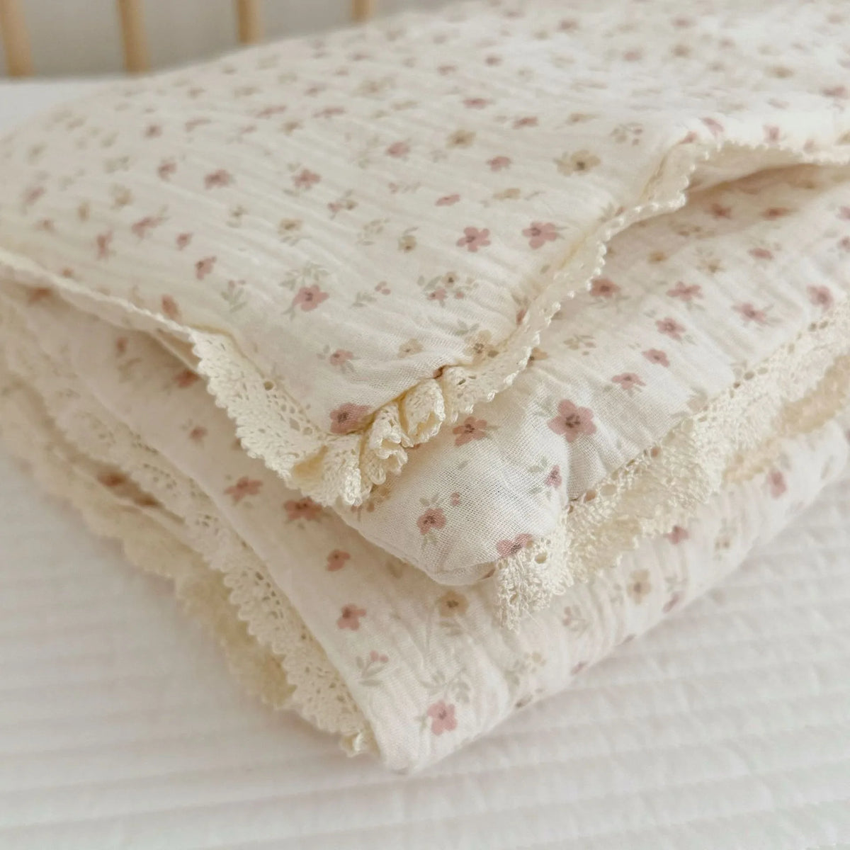 A stack of white muslin blankets with a delicate floral print resting on a white surface.