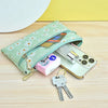 A light green PU leather coin purse with a wrist strap is shown next to a smartphone and a set of keys on a wooden surface.