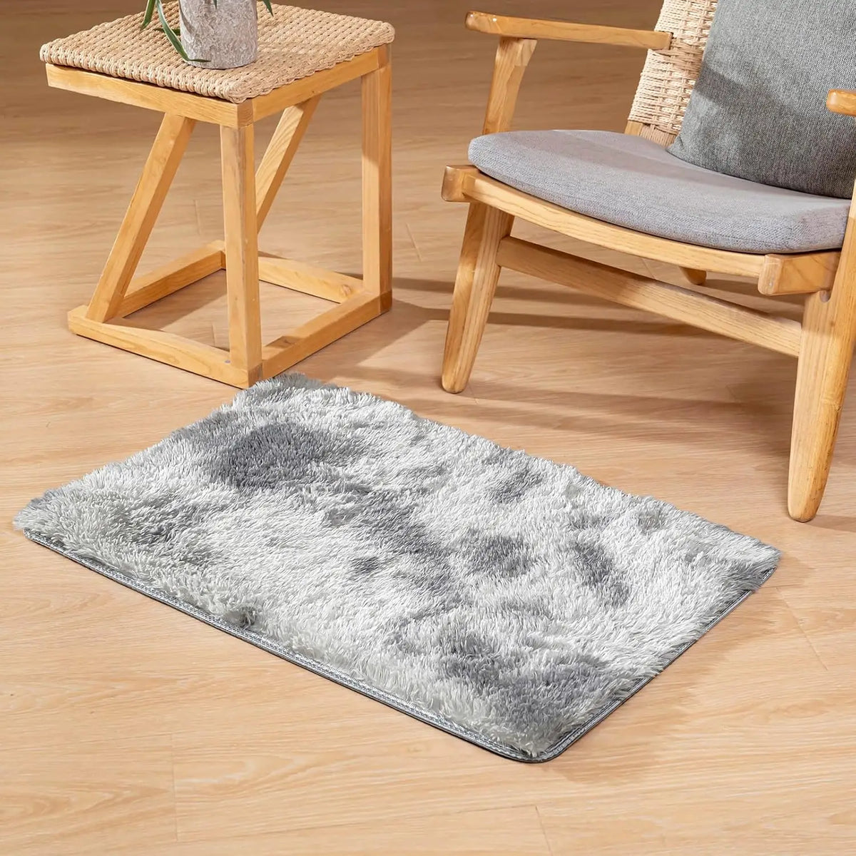 A gray faux fur area rug placed on a light wood floor next to a wooden chair and stool.