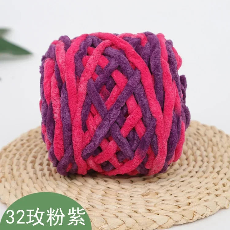A ball of magenta and purple chenille knitting yarn resting on a woven straw mat.