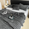 A gray ultra-soft plush winter blanket draped over a white bed with dark pillows and a black headboard.