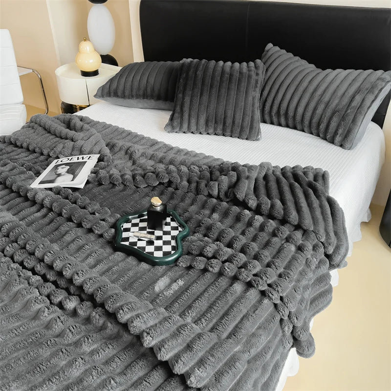 A gray ultra-soft plush winter blanket draped over a white bed with dark pillows and a black headboard.