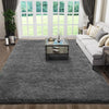 A gray plush floor mat placed on a wooden floor in front of a large window with greenery visible outside.