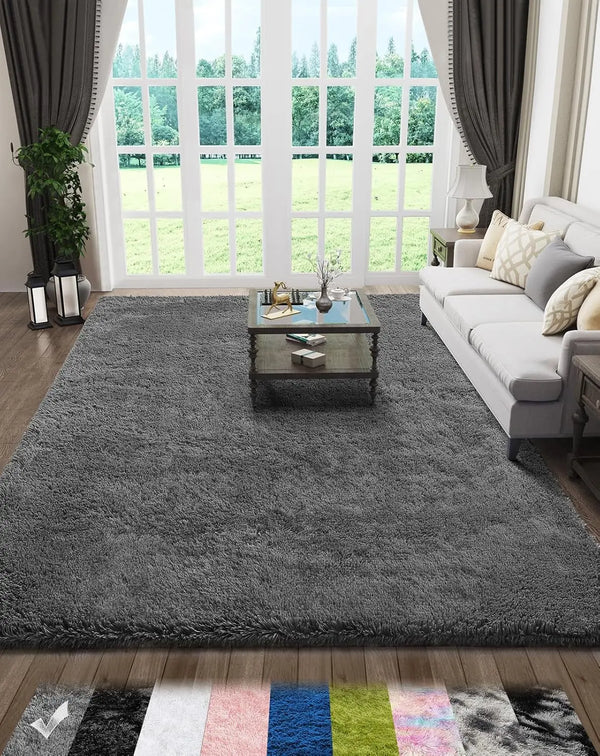 A gray plush floor mat placed on a wooden floor in front of a large window with greenery visible outside.