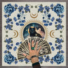 A hand holds a stack of tarot cards surrounded by blue and purple floral elements and crescent moons.