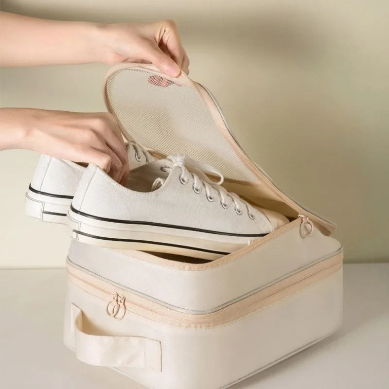 A hand opens a beige portable travel shoe organizer bag revealing a pair of white sneakers.