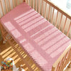 A pink soft plush mattress and diaper changing cover laid out inside a wooden crib.
