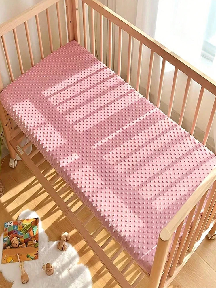 A pink soft plush mattress and diaper changing cover laid out inside a wooden crib.