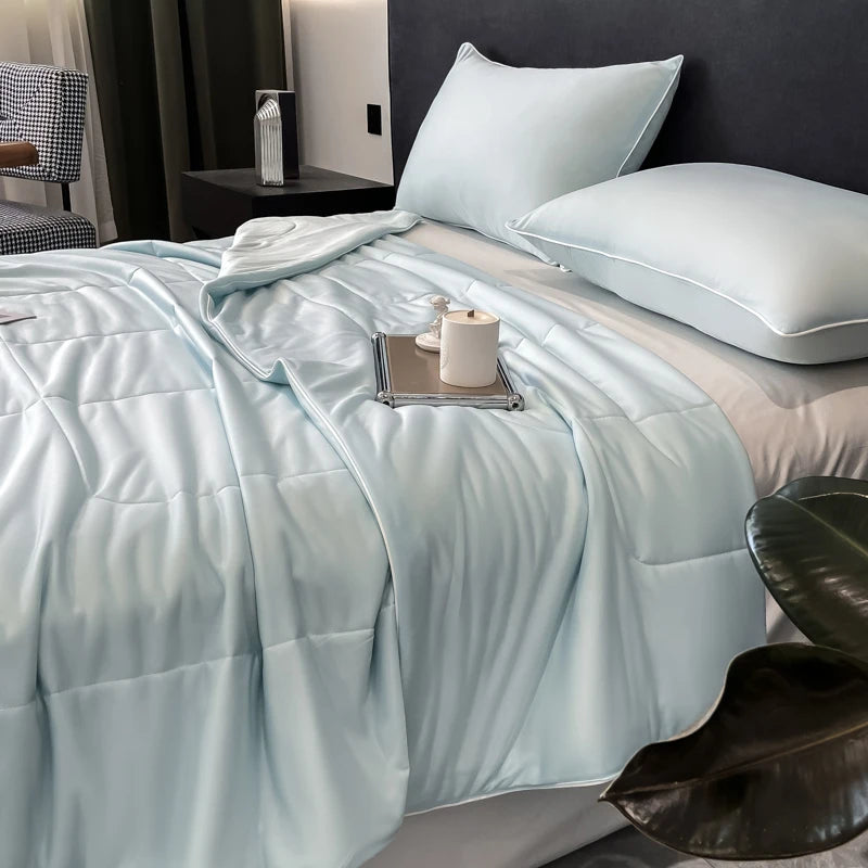 A light blue quilted blanket is spread on a bed, with a white pillow and a small candle resting on the fabric.