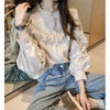 A woman models a cream lace long sleeve blouse and blue jeans in a studio setting.