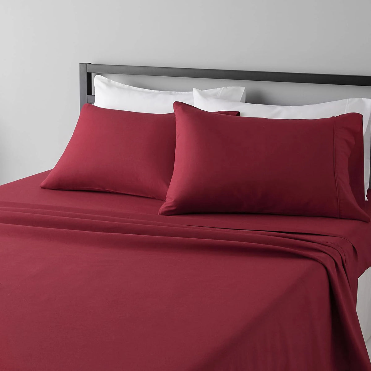 A set of four red microfiber flat fitted sheets on a bed with white pillows.