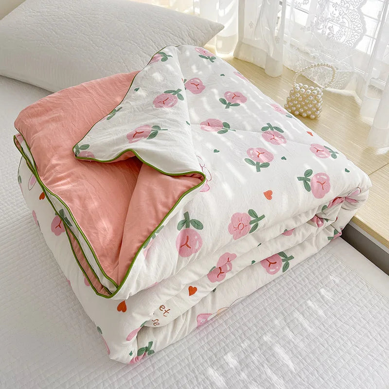 A white quilt with pink floral embroidery and a pink lining is folded on a light-colored surface.