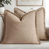 A beige linen throw pillow with fringed edges resting on a light gray sofa.