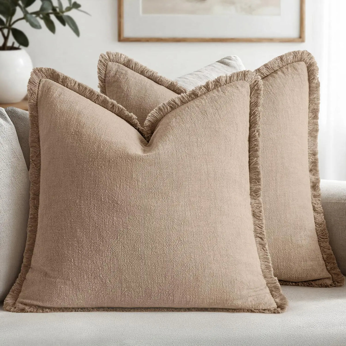 A beige linen throw pillow with fringed edges resting on a light gray sofa.