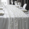 A white pearl beaded tulle table runner draped elegantly on a white tablecloth for an event.