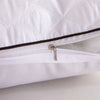 A close-up of a white quilted sleeping pillow with a zippered opening and a metallic pull tab.