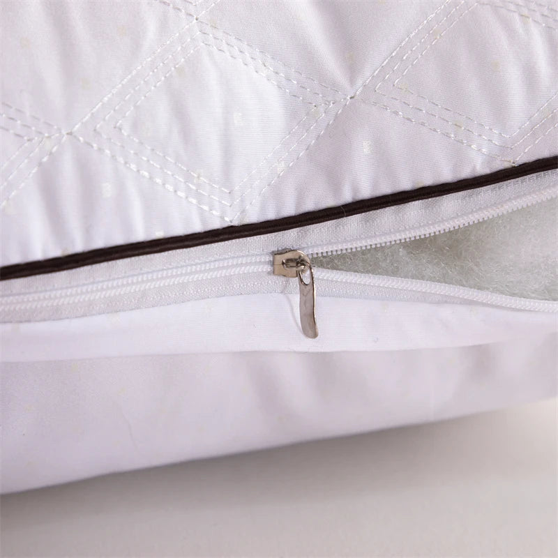 A close-up of a white quilted sleeping pillow with a zippered opening and a metallic pull tab.