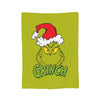 A green throw blanket featuring a cartoon grinch character wearing a red Santa hat.