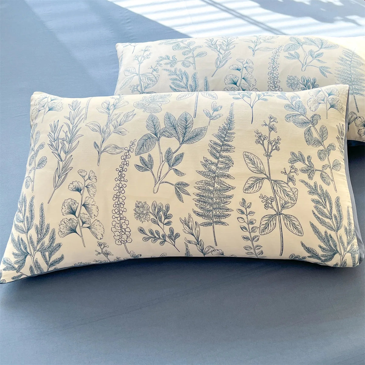 A close-up of a light blue floral printed pillow cover with delicate botanical illustrations on a blue surface.