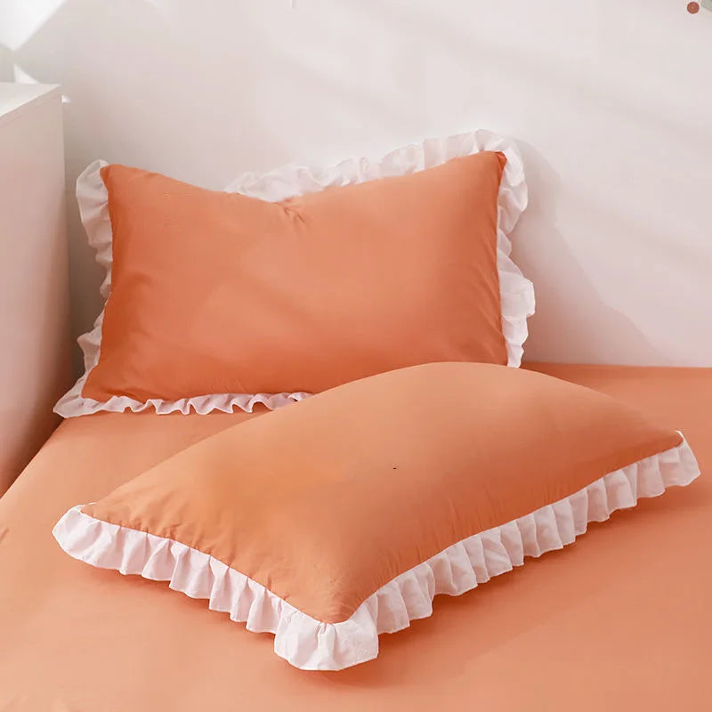 A pair of ruffled peach colored pillowcases with a white trim and hidden zipper on a bed.