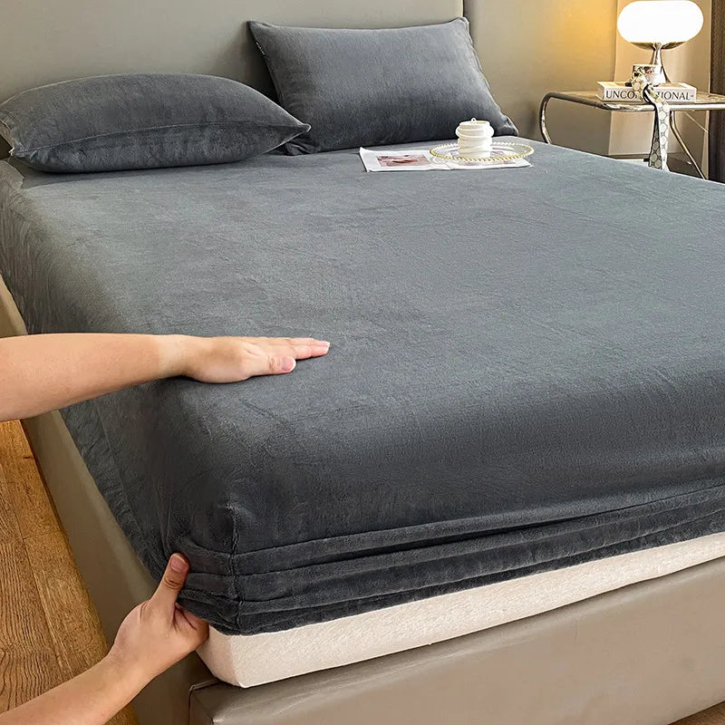 A hand is folding a dark gray luxury velvet bedding set onto a bed.