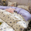A bed with pink floral bedding set featuring white and purple fabrics and a stuffed animal pillow.