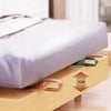 A wooden mattress lifter wedge is shown lifting a white pillow or bedding for easy changes.