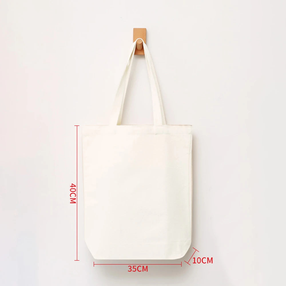 A white reusable canvas tote bag hanging by its handle against a white background.