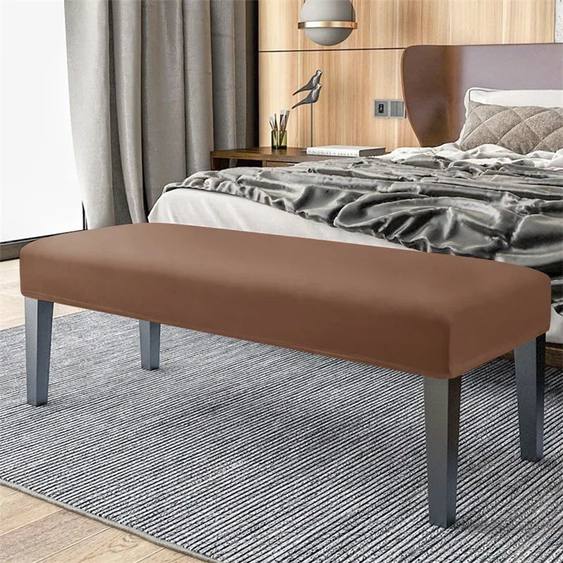 A rectangular brown velvet bench slipcover with gray legs placed on a striped rug in a bedroom setting.
