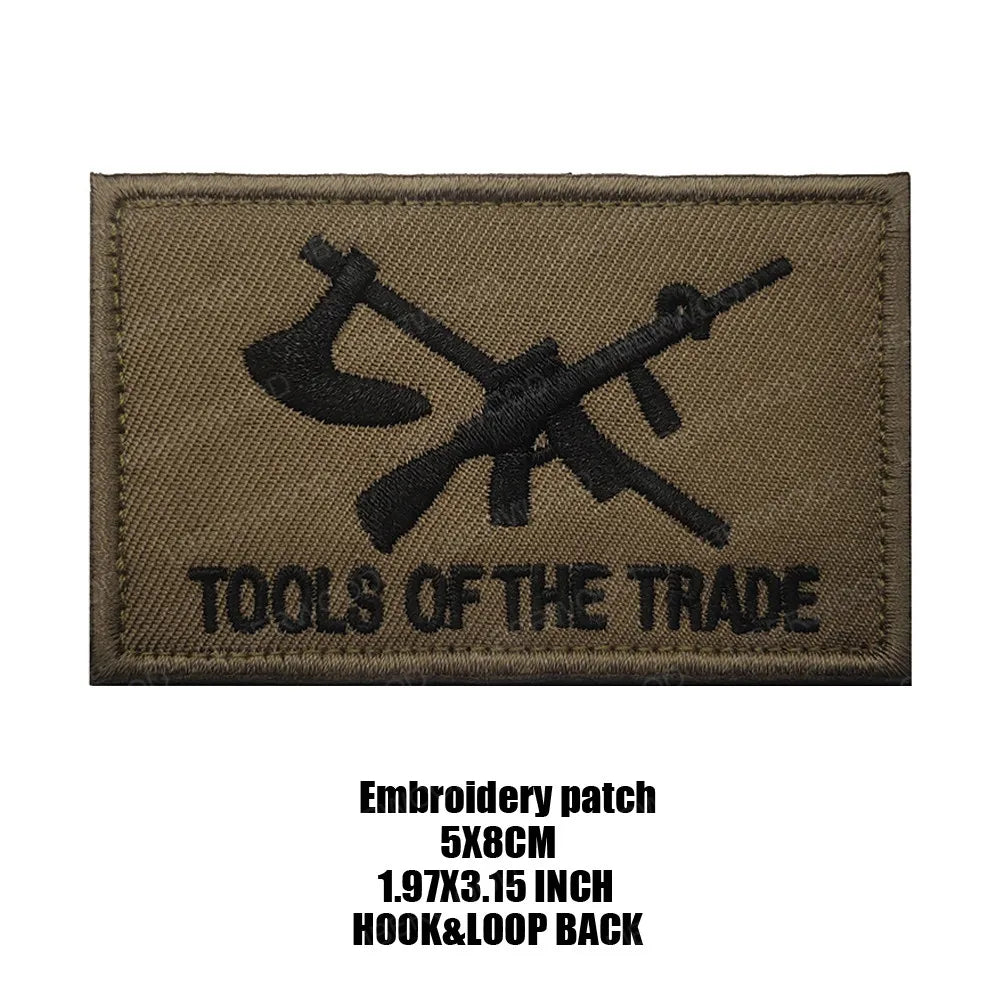 A dark olive green embroidered patch with the text TOOLS OF THE TRADE on it.