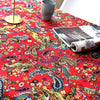 A close-up of a red bohemian printed linen fabric with floral and paisley patterns on a table.