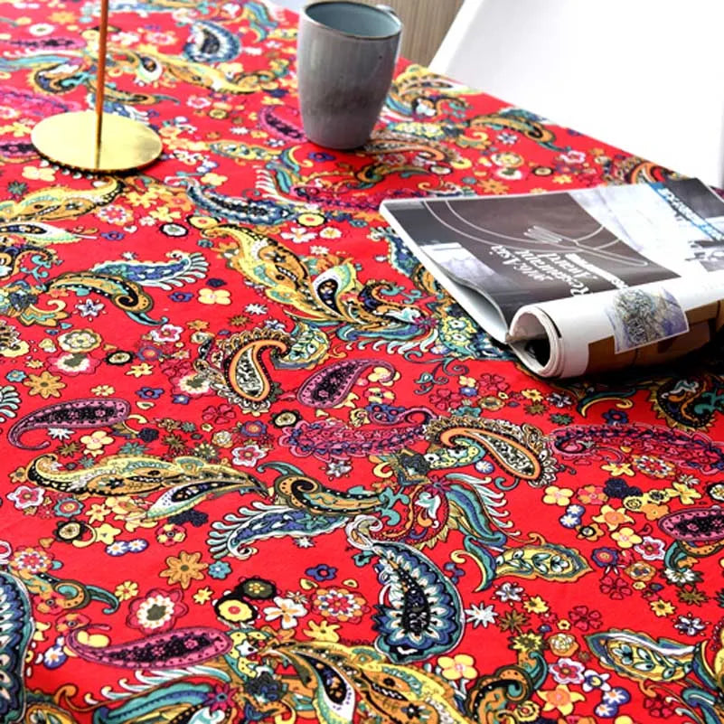A close-up of a red bohemian printed linen fabric with floral and paisley patterns on a table.