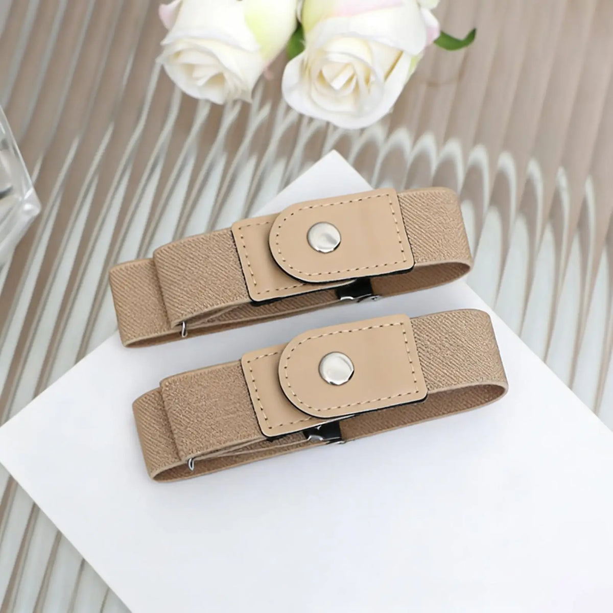A beige stretchable elastic belt with a leather-look buckle is displayed on a white surface.