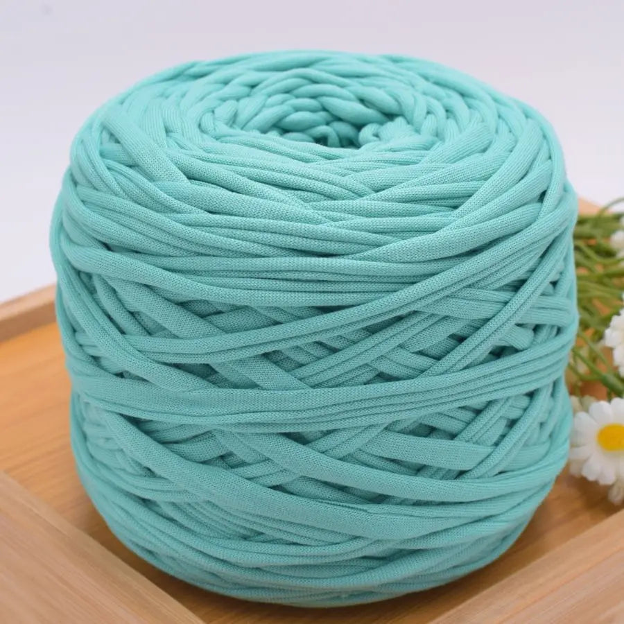 A ball of teal green craft yarn for knitting and DIY displayed on a wooden surface.
