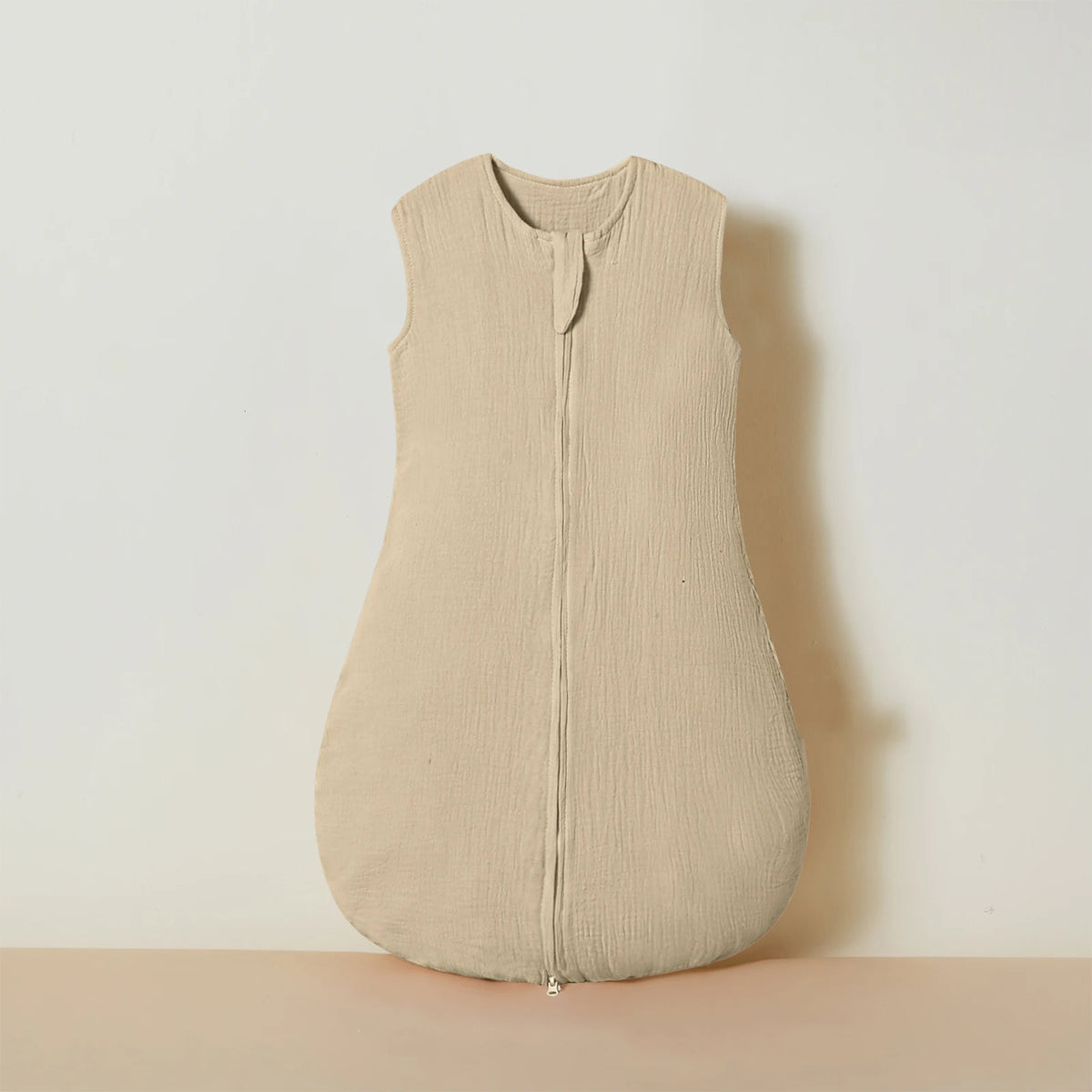 A beige muslin cotton baby sleeping bag with a front zipper, displayed against a light background.