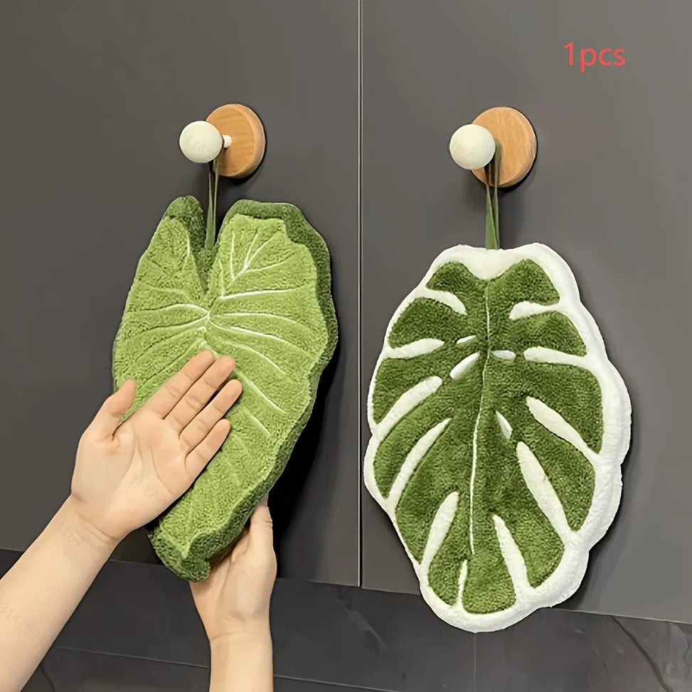 A hand towel shaped like a leaf is hanging on a wooden hook against a dark gray background.