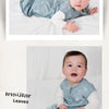 A baby wearing a light blue patterned cotton sleep sack lying on white bedding.