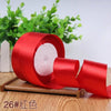 A roll of red satin ribbon for gift wrapping and DIY crafts placed on a wooden surface with green foliage in the background.