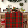A red tartan Christmas table runner displayed on a wooden table with holiday decorations.