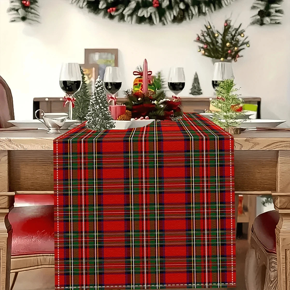 A red tartan Christmas table runner displayed on a wooden table with holiday decorations.
