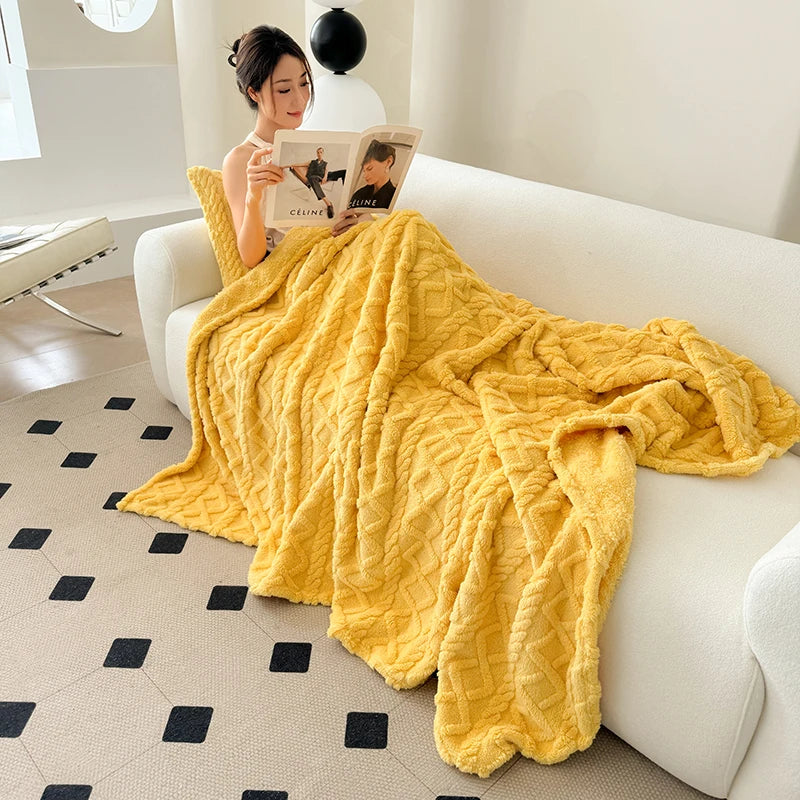 A bright yellow ultra-soft coral fleece blanket draped over a white sofa with a woman reading a magazine nearby.