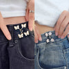 Close-up of a hand adjusting an adjustable alloy button clip for tightening the waist of dark denim jeans.