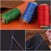 Rolls of waxed thread in green, blue, and red next to a sewing needle drawing lines on black fabric.