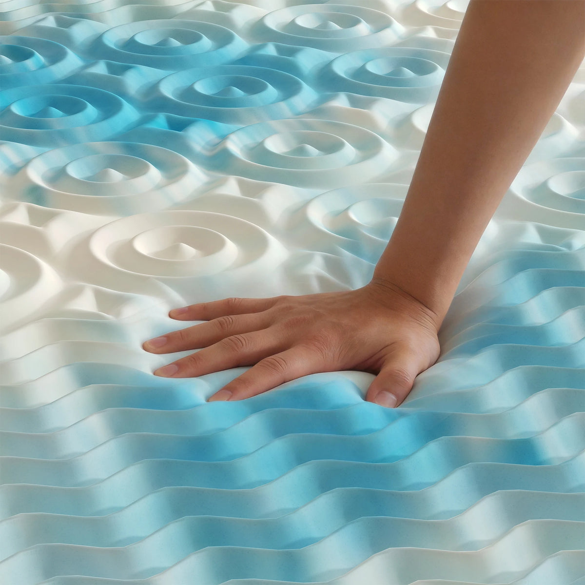 A hand rests on a blue memory foam mattress topper featuring a wavy, patterned surface.