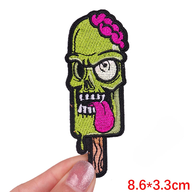 A hand holds a embroidered patch of a skull with pink roses on a wooden stick.