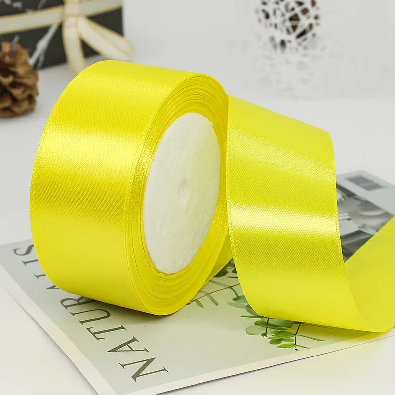 A roll of bright yellow satin ribbon with white filling, lying on a piece of paper.